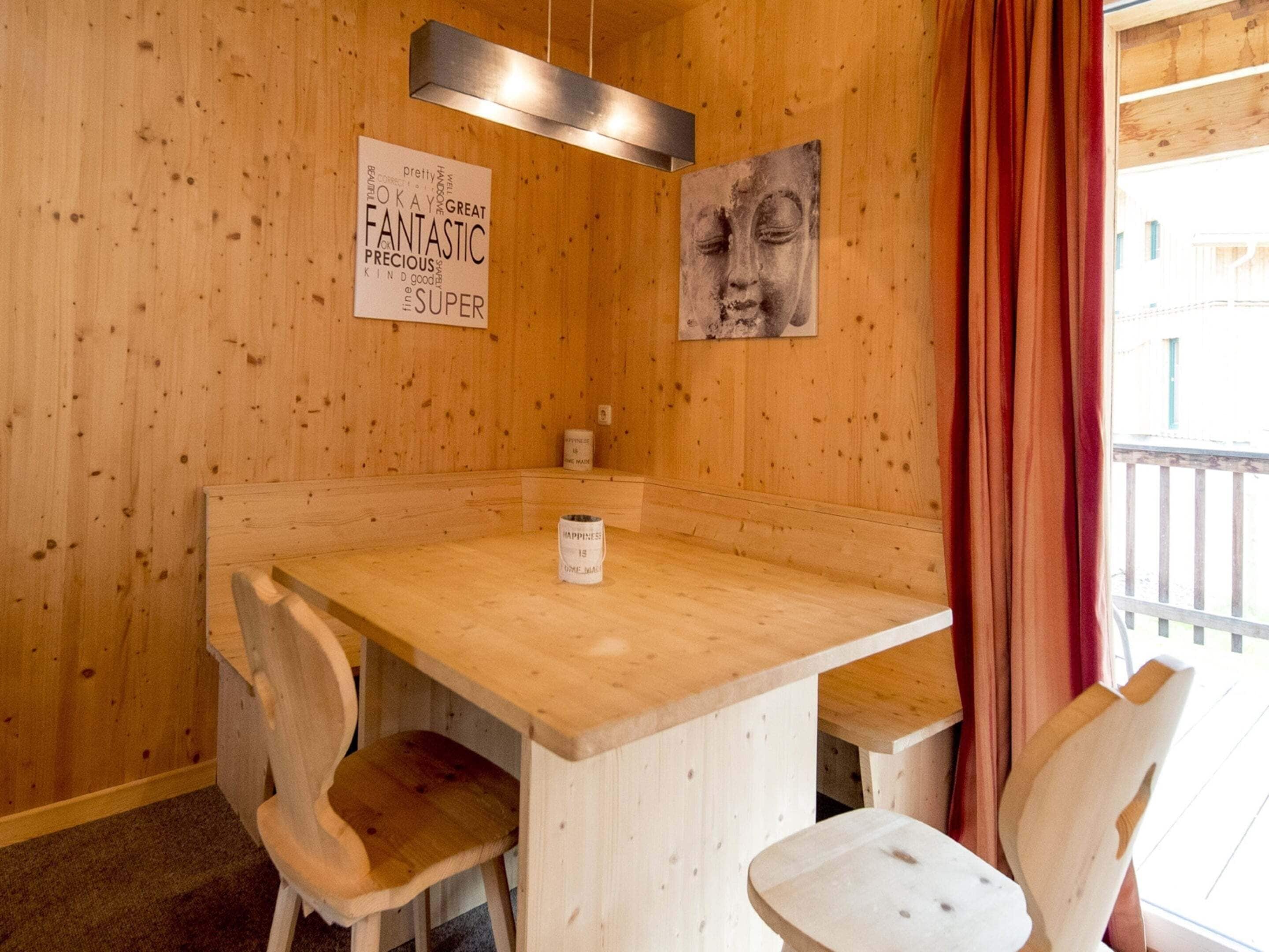 Un interior de fusta amb una taula i cadires, un cartell amb paraules positives i una finestra amb cortines.