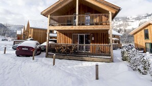 A wooden chalet with a balcony, surrounded by snow-covered ground and parked cars. - Amazing House With Balcony (Sankt Georgen am Kreischberg)