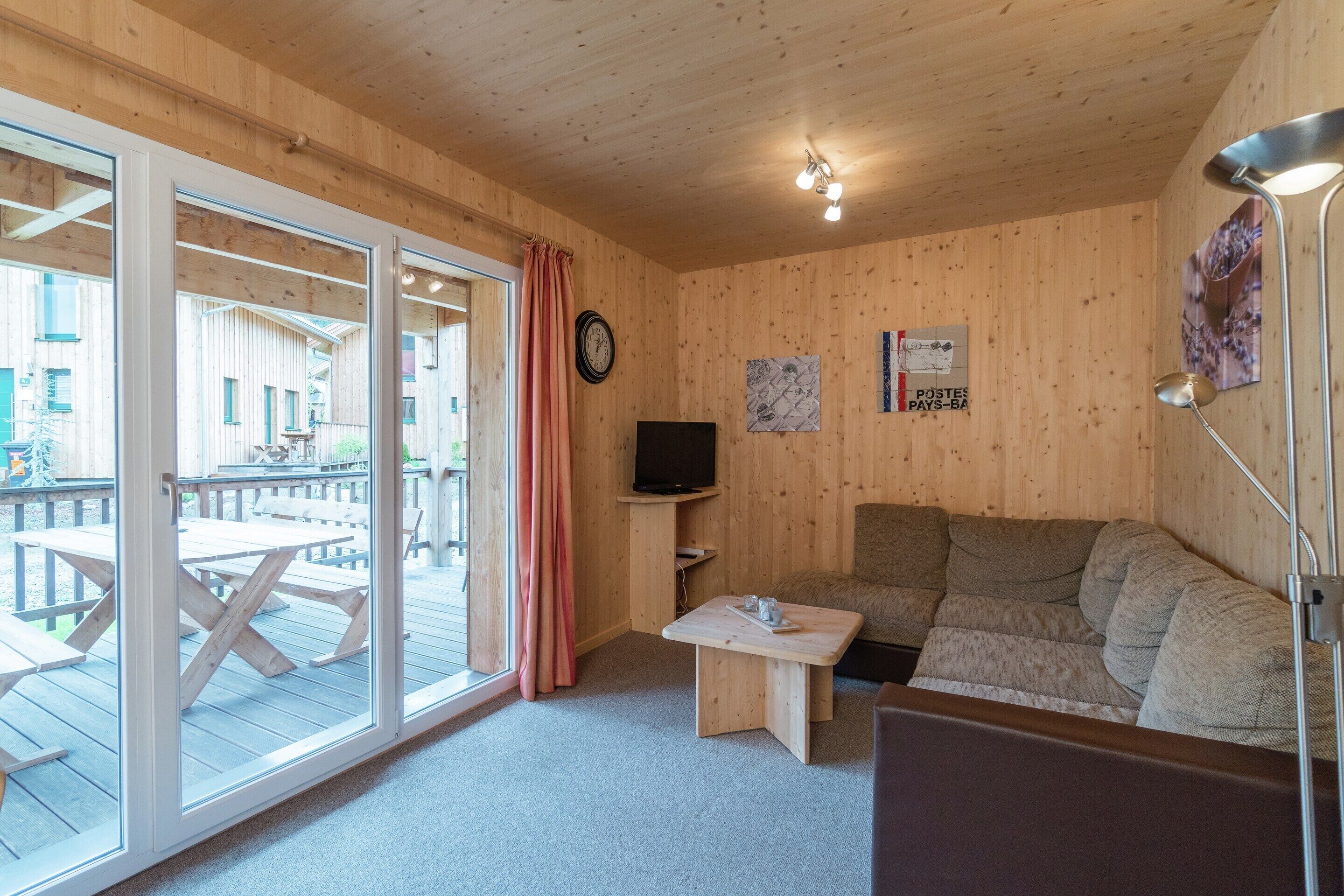 Un intérieur en bois avec un canapé, une petite table, un téléviseur et une grande fenêtre.