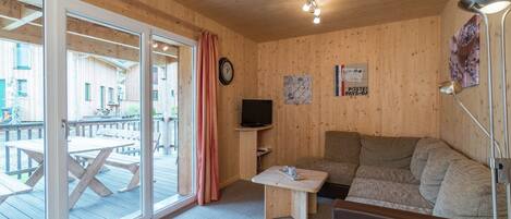 Un intérieur en bois avec un canapé, une petite table, un téléviseur et une grande fenêtre.