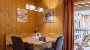 A wooden interior with a wooden table, two chairs, a pendant light, a framed quote, and a view of the outside deck. - Amazing House With Balcony (Sankt Georgen am Kreischberg)