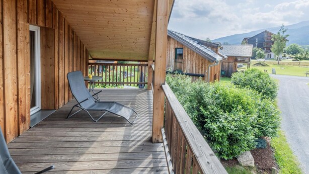 A wooden deck with a lounge chair, a view of a mountain, and a building with a sloped roof. - Amazing House With Balcony (Sankt Georgen am Kreischberg)