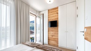 Un dormitorio moderno con una cama grande, un panel de madera decorativo, una puerta corredera a un balcón y un televisor montado.