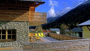 A chalet with a stone facade, wooden balcony, and a view of a mountain range. - Posh Mansion in Sankt with 2 Saunas, Whirlpool, Hot Tub (Sankt Anton am Arlberg)