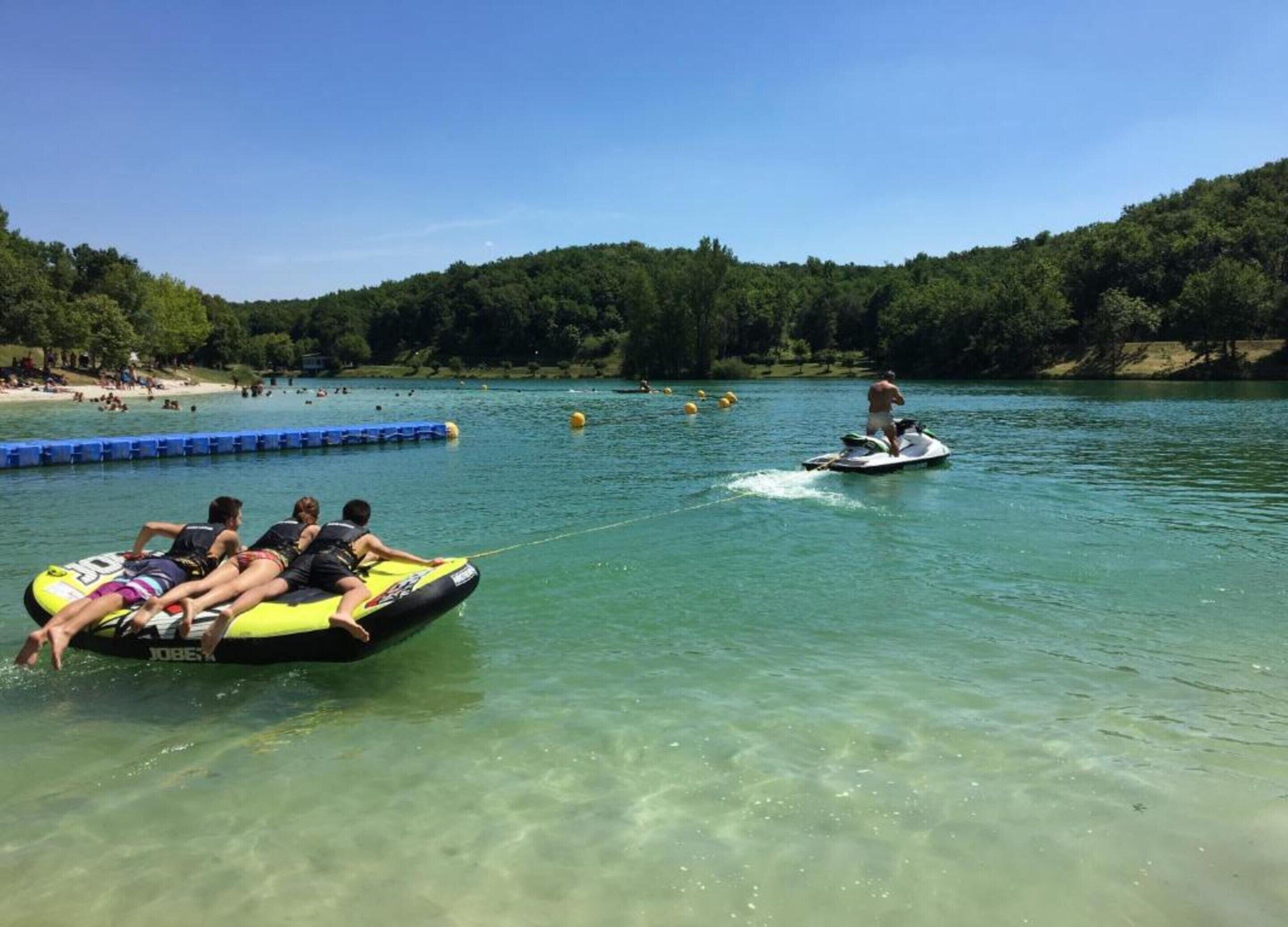 A lake with clear water, surrounded by trees and a sandy beach.