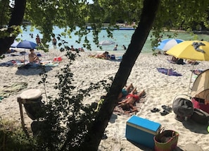 A beach with people sunbathing, umbrellas, and a cooler on the sand. - Holiday Home Montaigu-de-quercy Lake (Montaigu-de-Quercy)