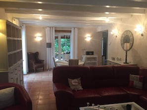 A living room with a red leather sofa, a coffee table, a dining area with a table and chairs, and a kitchen area with a refrigerator. - Holiday Home Montaigu-de-quercy Lake (Montaigu-de-Quercy)
