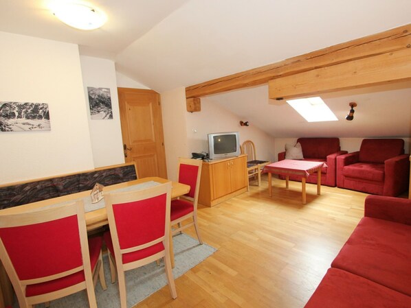 A cozy living room with a dining area, red furniture, a television, and a wooden ceiling.