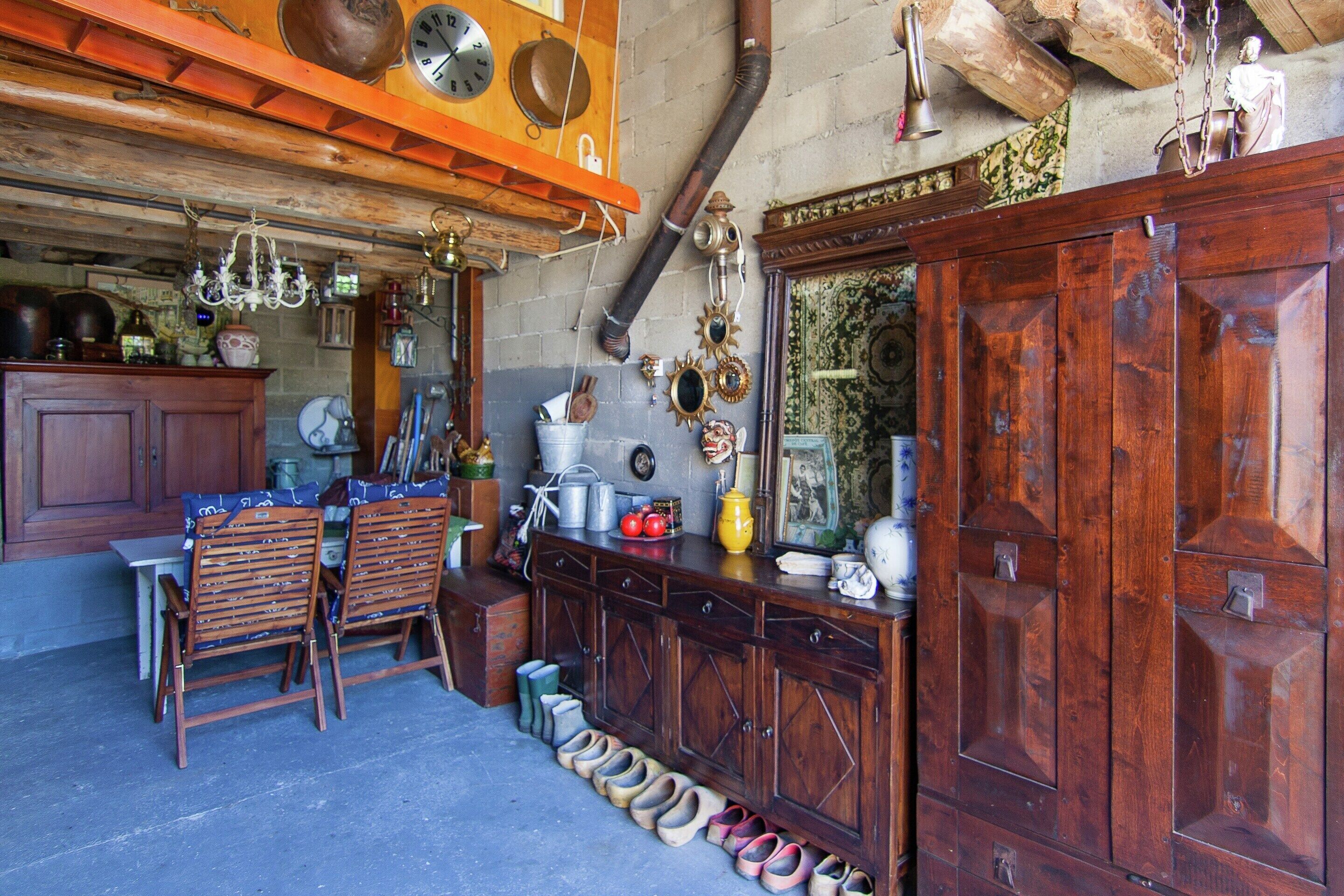 Um interior rústico com móveis de madeira, diversos objetos decorativos e uma coleção de sapatos expostos no chão.