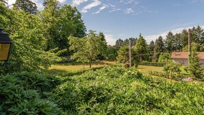A lush garden with various plants and trees, a lamp post, and a building with a tiled roof in the background. - Cottage Bliss in Roussines (Roussines)