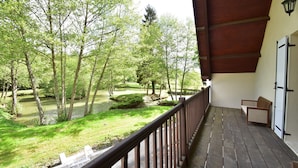 A wooden deck with a railing overlooking a garden with trees and a pond. - Charming Holiday Home With Pool and Pond (Villentrois-Faverolles-en-Berry)