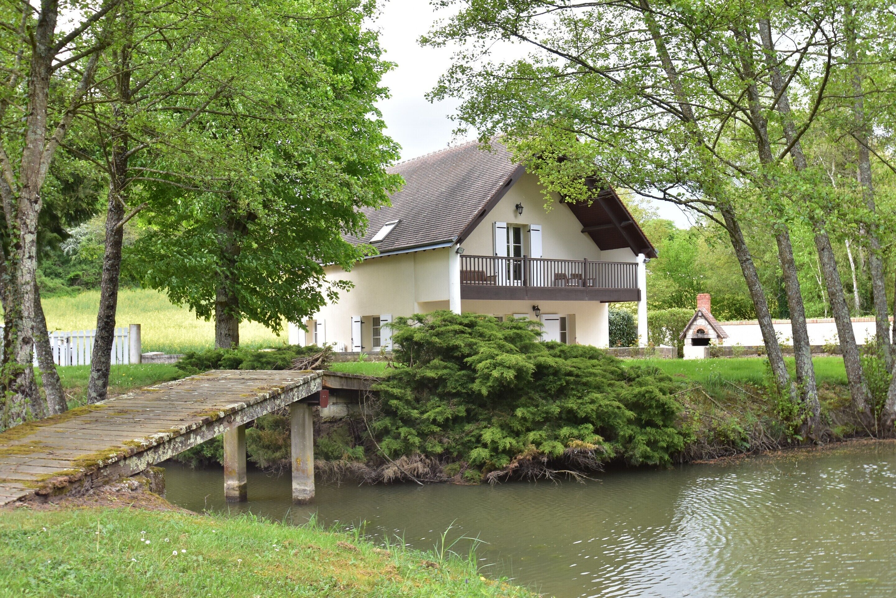 Une maison avec un balcon, un pont en bois et un étang.