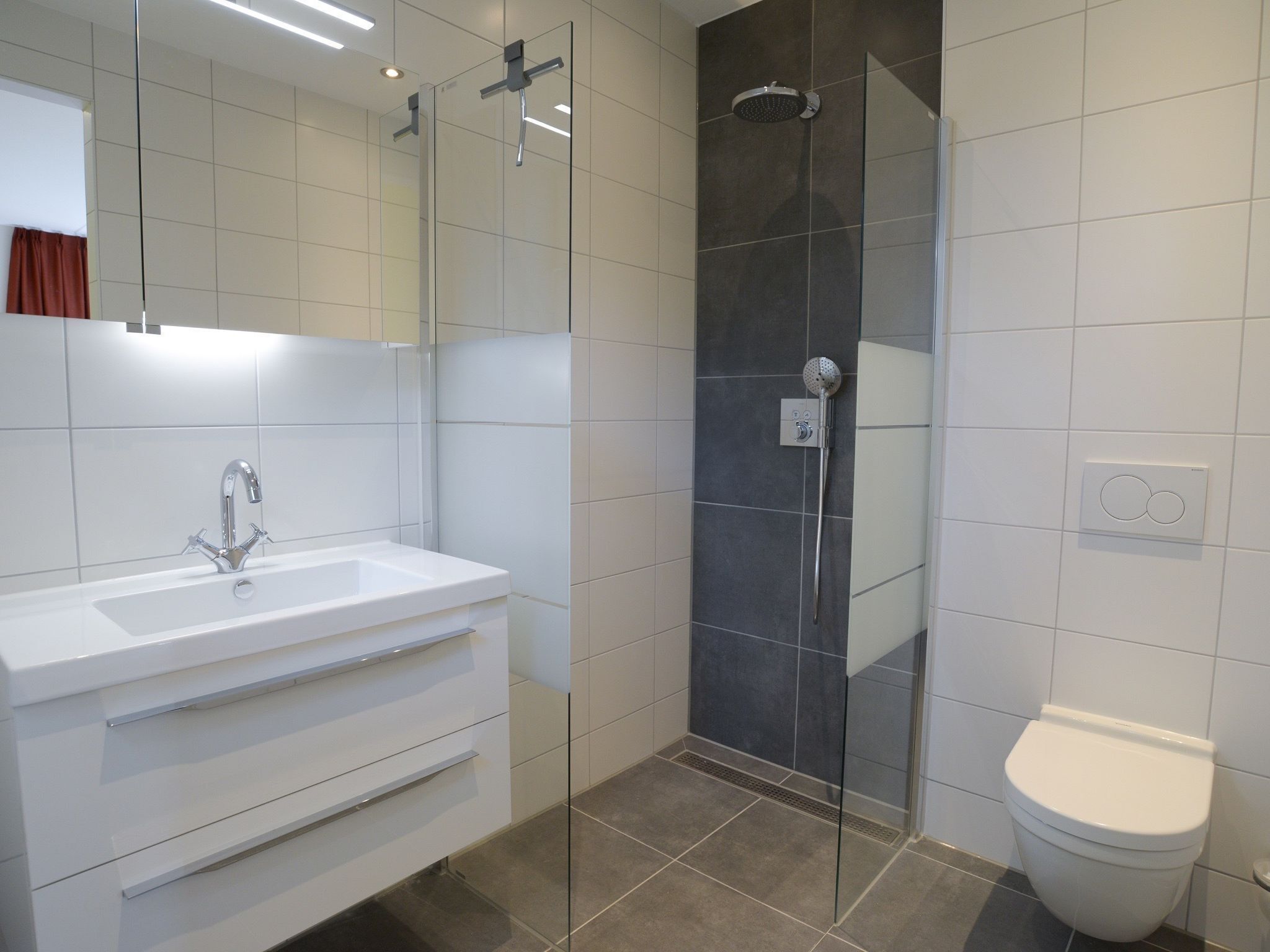 A modern bathroom with a white vanity, a glass shower enclosure, and a toilet.