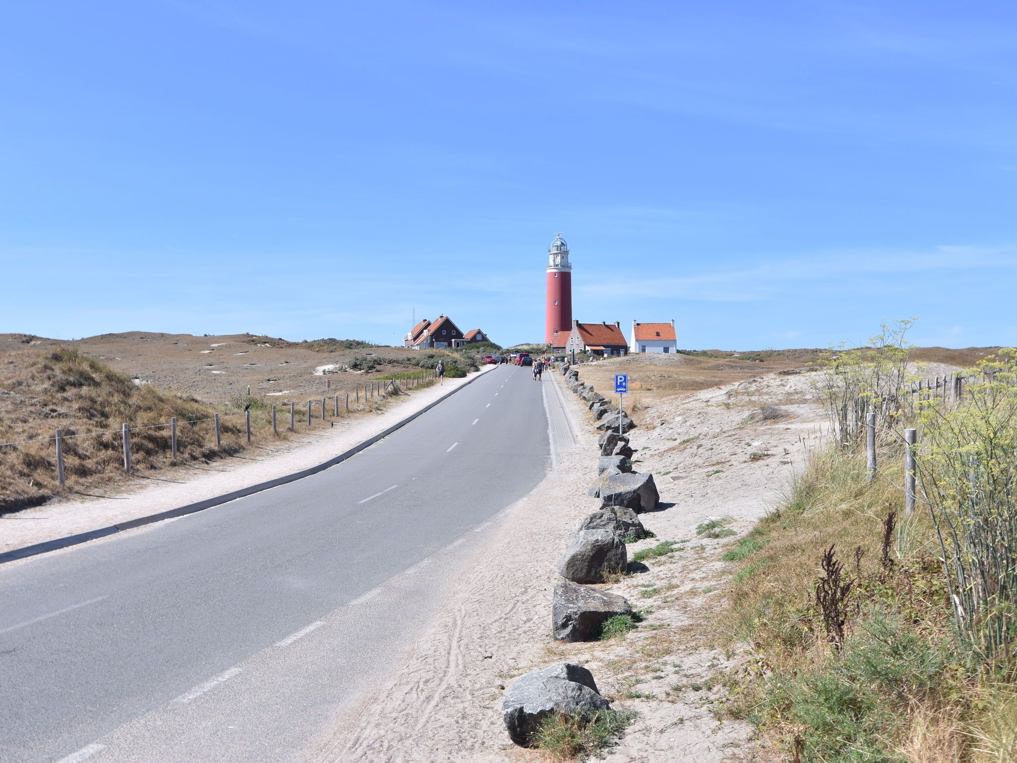 A coastal road with a lighthouse, houses, and a clear sky.