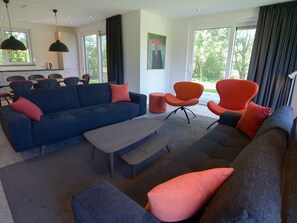 A modern living room with a blue sofa, orange armchairs, and a grey ottoman. - Peaceful Villa in De Koog near Sea (De Koog)