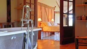 A bathroom with a bathtub, a shower, and a sink. There is a bed with pillows and a bedside table in the adjacent room. - Beautiful Farmhouse With Private Pool (Perchede)