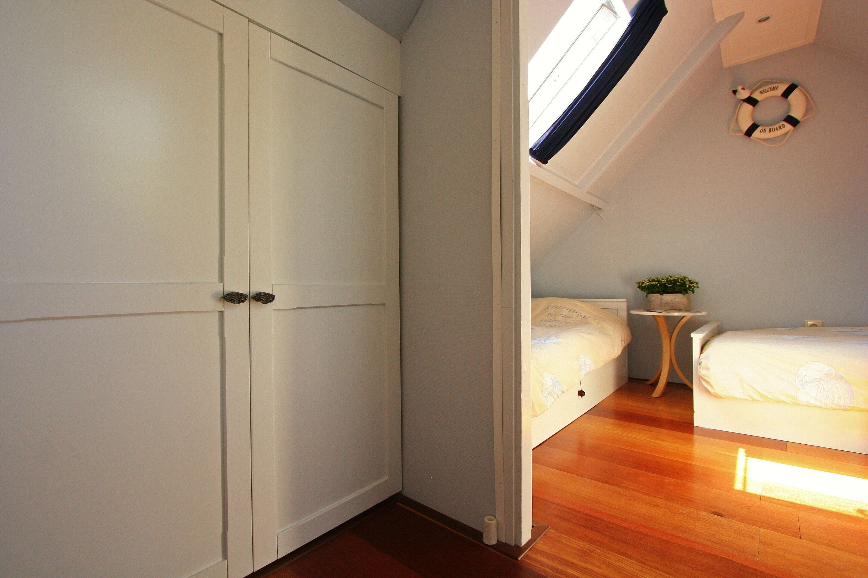 Un dormitorio con piso de madera, una cama, una mesita de noche con una planta y una lámpara en el techo.