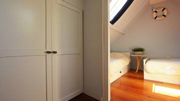 Un dormitorio con piso de madera, una cama, una mesita de noche con una planta y una lámpara en el techo.