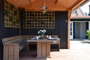 Eine Terrasse aus Holz mit einer Bank und einem Tisch, umgeben von dunklen Holzwänden und einer Reihe von Kübelpflanzen.