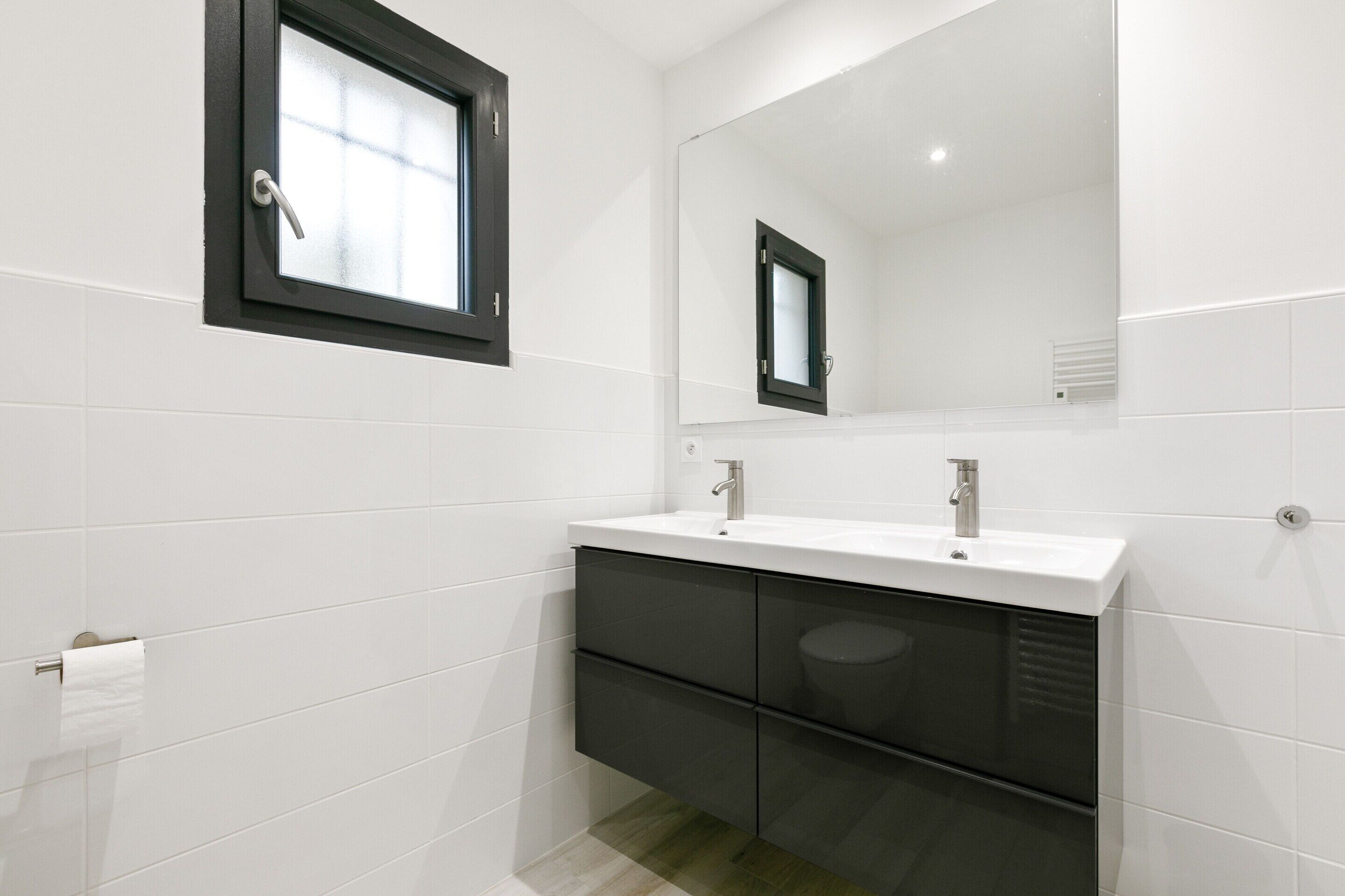 Un baño moderno con azulejos blancos, tocador doble y espejo sobre el lavabo.