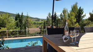 Um deck de madeira com piscina, uma garrafa de vinho e copos sobre uma mesa, com vista para a piscina e uma paisagem deslumbrante.