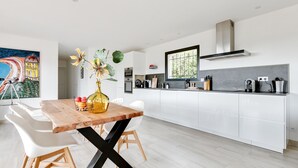 Una cocina moderna con armarios blancos, una mesa de comedor de madera y un ventanal grande.