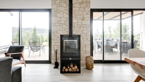 Una sala moderna con chimenea de piedra, ventanas amplias y mobiliario para exteriores.