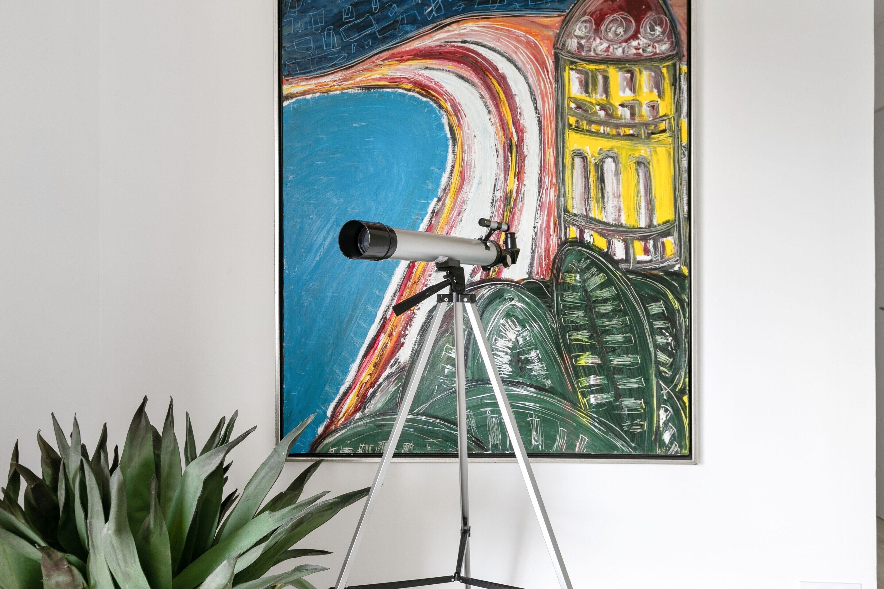 Een telescoop op een statief voor een kleurrijk abstract schilderij.
