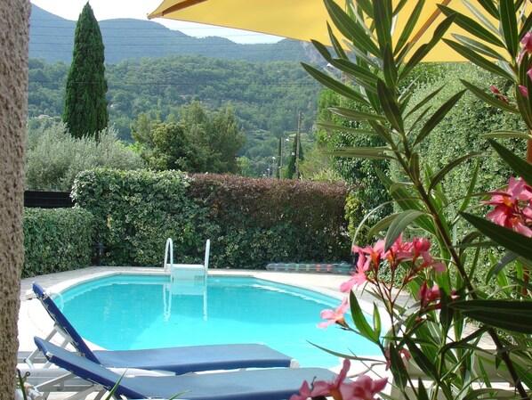 Una piscina con sillas de descanso y un paraguas amarillo, rodeada de vegetación y colinas.