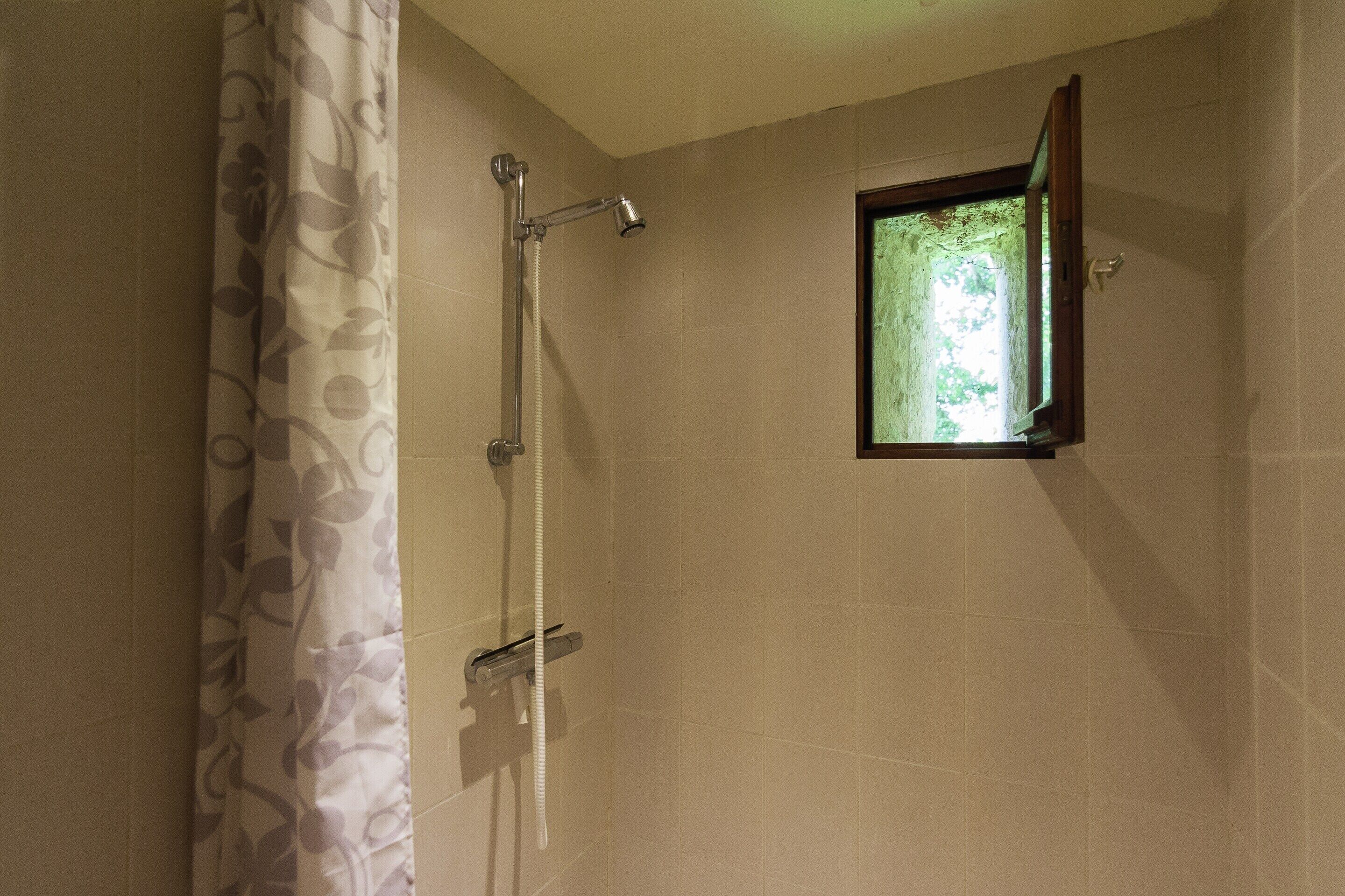 A shower with a curtain, a handheld showerhead, and a small window.