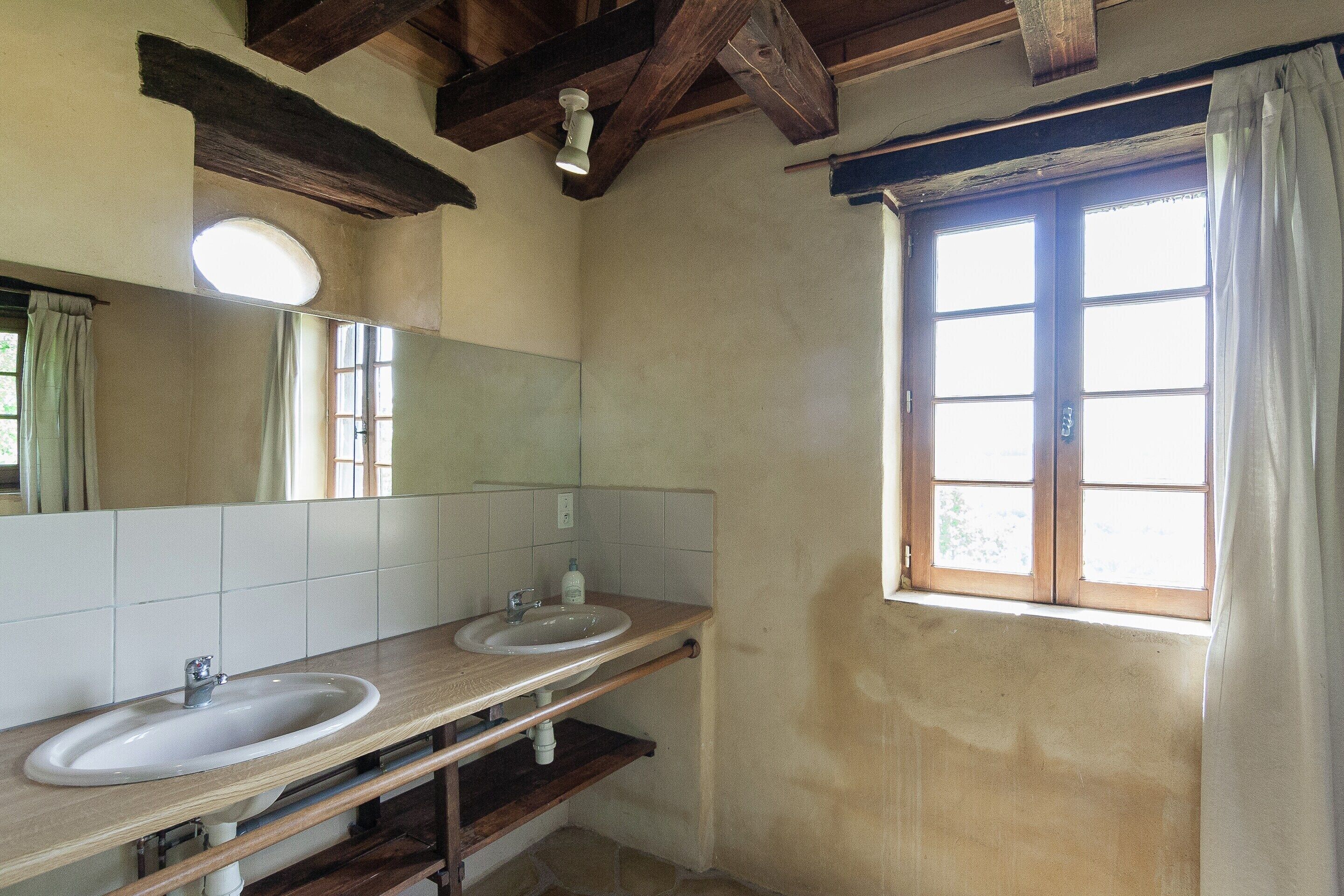 A bathroom with two sinks, a mirror, and a window with curtains.