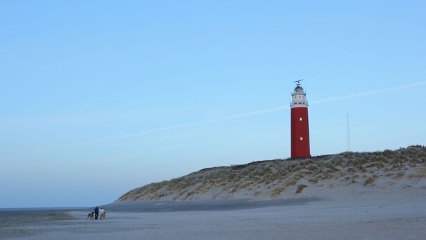 Um farol numa praia de areia sob um céu claro.
