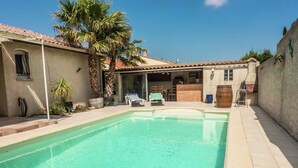 A swimming pool with a tiled deck, a covered patio area, and a building with a tiled roof. - Chic Narbonne Pool Retreat (Narbonne)