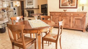 A dining area with a wooden table, chairs, a fireplace, a television, and a kitchen in the background. - Chic Narbonne Pool Retreat (Narbonne)