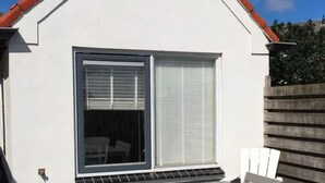 Ein modernes Haus mit weißer Fassade, einem roten Ziegeldach und einem großen Fenster mit weißem Rollo.