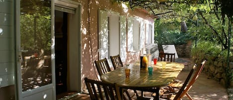 An outdoor dining area with a table and chairs, a stone wall, and a door leading to a covered space.
