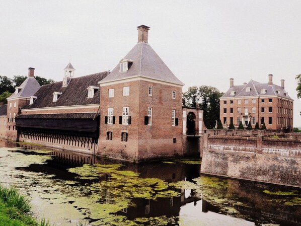 A historic building with a large brick structure, a water canal in front, and a bridge connecting to another building.
