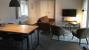 A modern living room with a wooden dining table, two sofas, a TV, and a small side table. - Peaceful Forest Chalet (Elst)