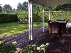 A covered outdoor seating area with a wooden deck, white pillars, and wicker furniture.