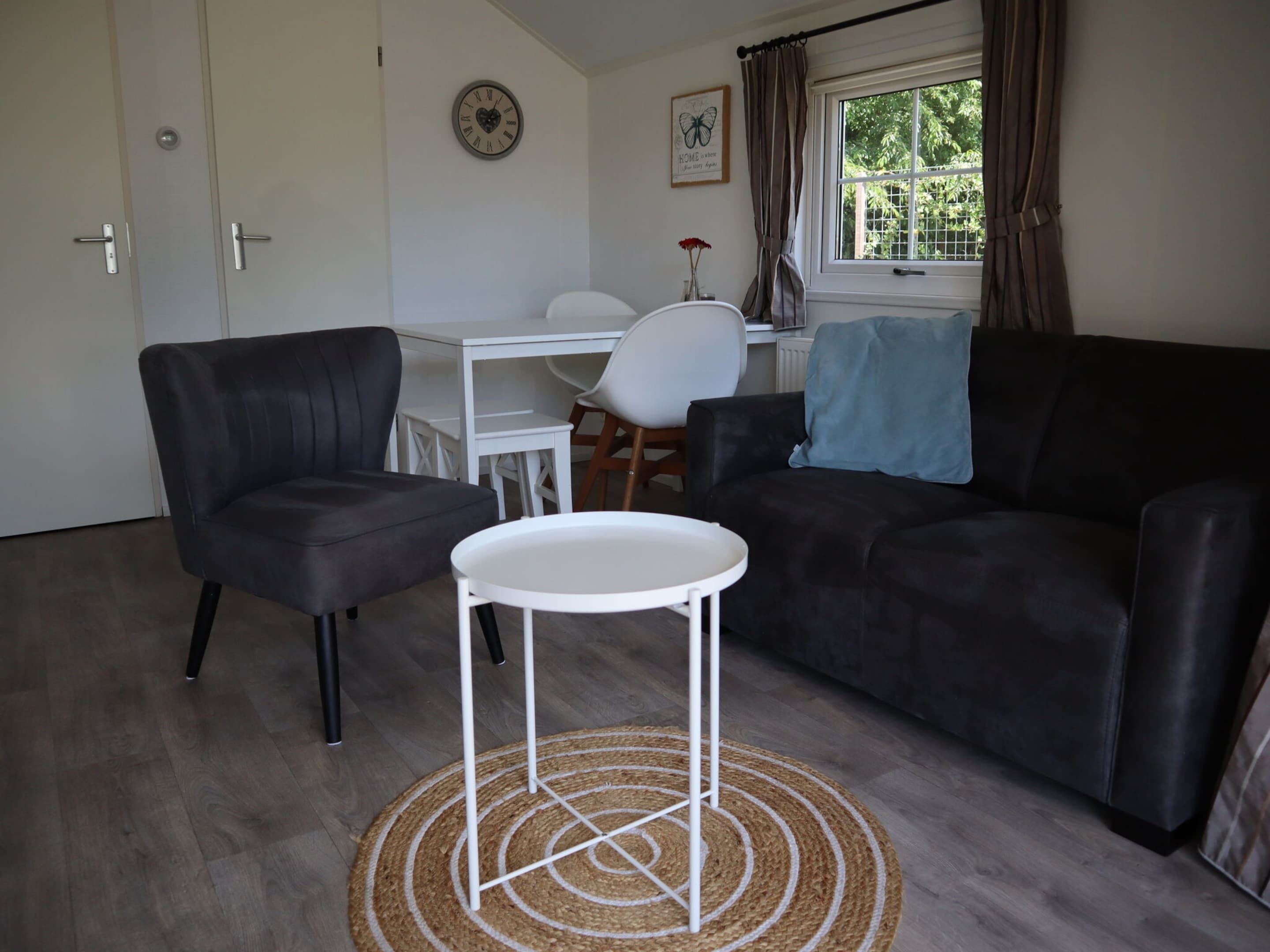 A modern living room with a black leather sofa, a white round table, and a white desk.