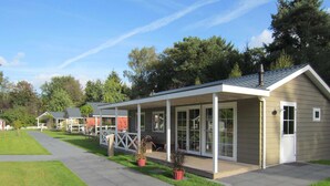 A modern single-story building with a covered patio area, a small garden, and a paved walkway. - Houses Toger With Group Space in 't Vechtdal (Dalfsen)