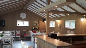 A spacious kitchen with a wooden ceiling, a dining area with white chairs, and a bar counter. - Houses Toger With Group Space in 't Vechtdal (Dalfsen)