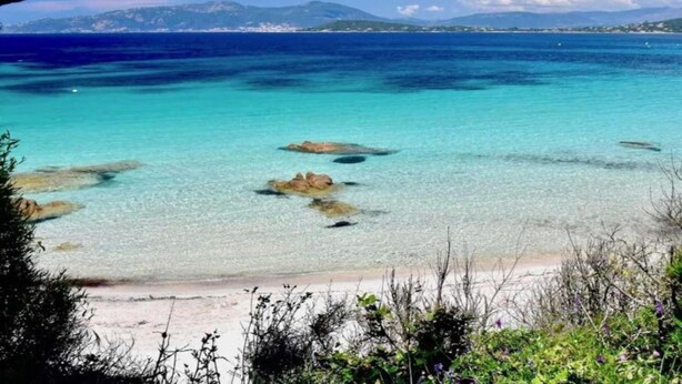 A beach with clear turquoise water, rocky outcrops, and distant mountains. - Peaceful Getaway in Nature (Varsberg)