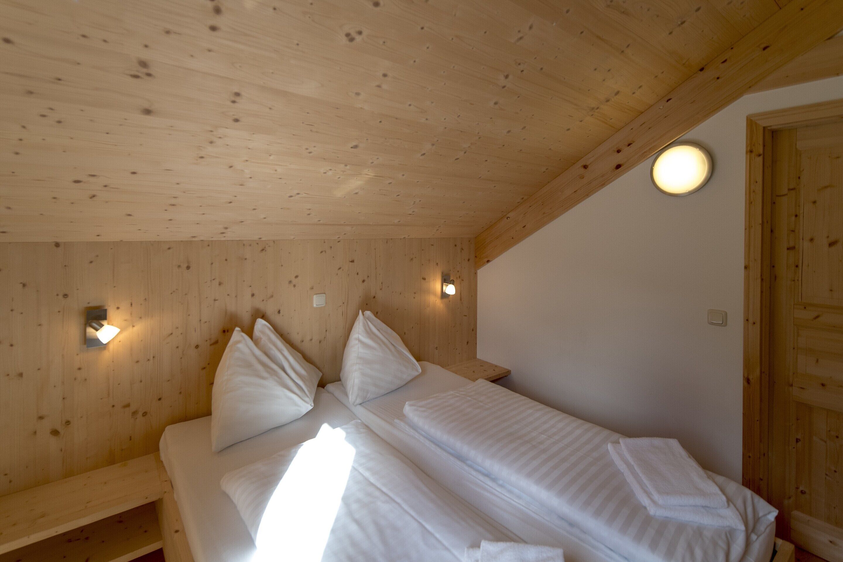 A wooden cabin room with two beds, wooden walls, and a ceiling light.