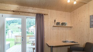 Een kamer met houten inrichting, een schuifdeur van glas naar een buitenterras, een tafel met tijdschriften en een stoel.