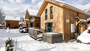 Een houten lodge met meerdere kamers, buiten zitplaatsen en een jacuzzi in een besneeuwde omgeving.