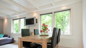A modern room with a wooden dining table, black chairs, a flat-screen TV mounted on the wall, and large windows with a view of greenery. - Elegant Apartment in Hoorn With Roof Terrace (Hoorn)