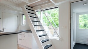 A modern kitchen with white cabinetry, a black countertop, and a wooden floor. A white staircase with black steps leads to a door with a black mat. - Elegant Apartment in Hoorn With Roof Terrace (Hoorn)