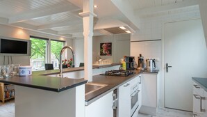 A modern kitchen with white cabinetry, a central island, stainless steel appliances, and a large window offering a view of the outdoors. - Elegant Apartment in Hoorn With Roof Terrace (Hoorn)