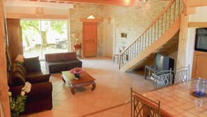 A living room with a sofa, coffee table, and TV. There's a staircase with a wooden railing. - Villa in Conilhac With Private Terrace (Roquetaillade-et-Conilhac)